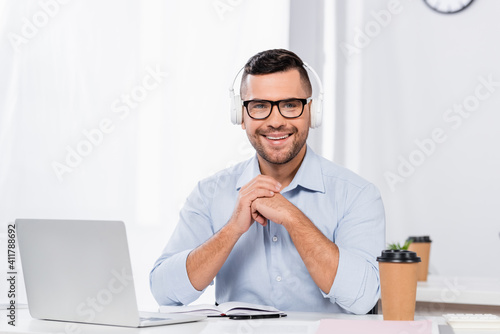 happy businessman in glasses and headphones smiling while looking at camera
