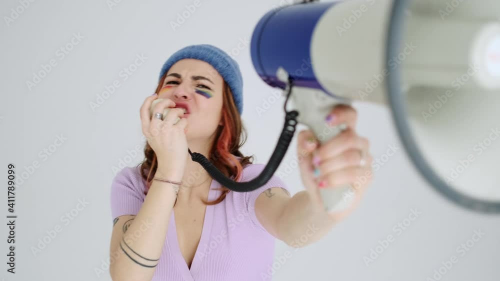 A cropped view of a happy young woman with a rainbow makeup is screaming to the shout standing isolated over gray background A cropped view of a happy young woman with a rainbow makeup is screaming to the shout standing isolated over gray background