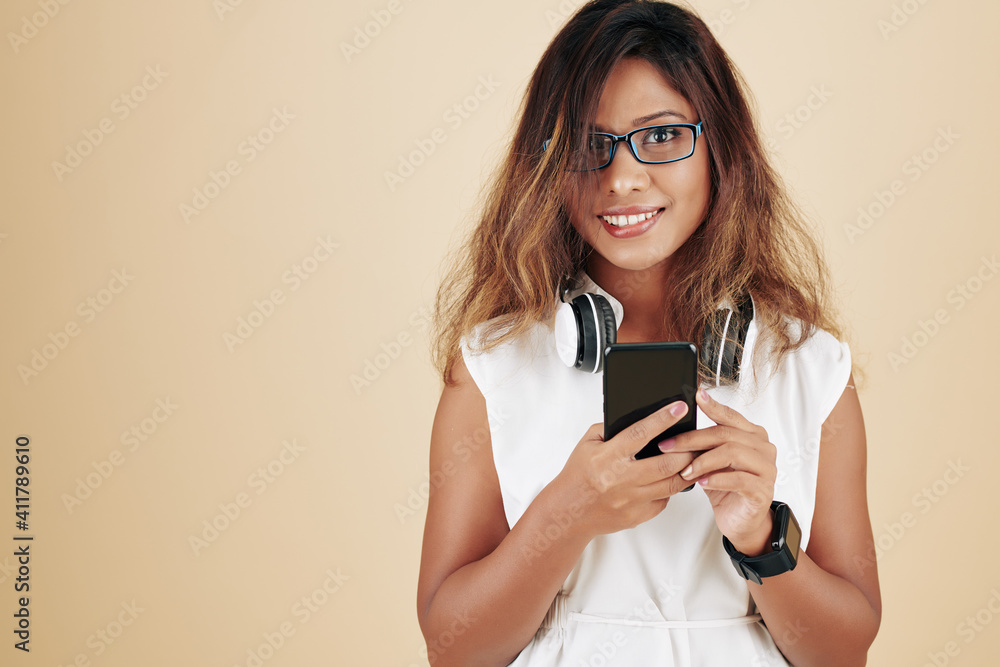 Portrait of cheerful young Asian woman in glasses choosing music on smartphone to listen to in headphones Portrait of cheerful young Asian woman in glasses choosing music on smartphone to listen to in headphones
