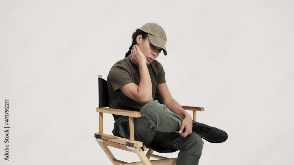 A calm young american soldier woman is sitting on the chair isolated over the gray background in the studio A calm young american soldier woman is sitting on the chair isolated over the gray background in the studio