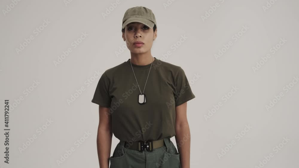 A serious young american soldier woman is standing in a confident pose isolated over a gray background in the studio A serious young american soldier woman is standing in a confident pose isolated over a gray background in the studio