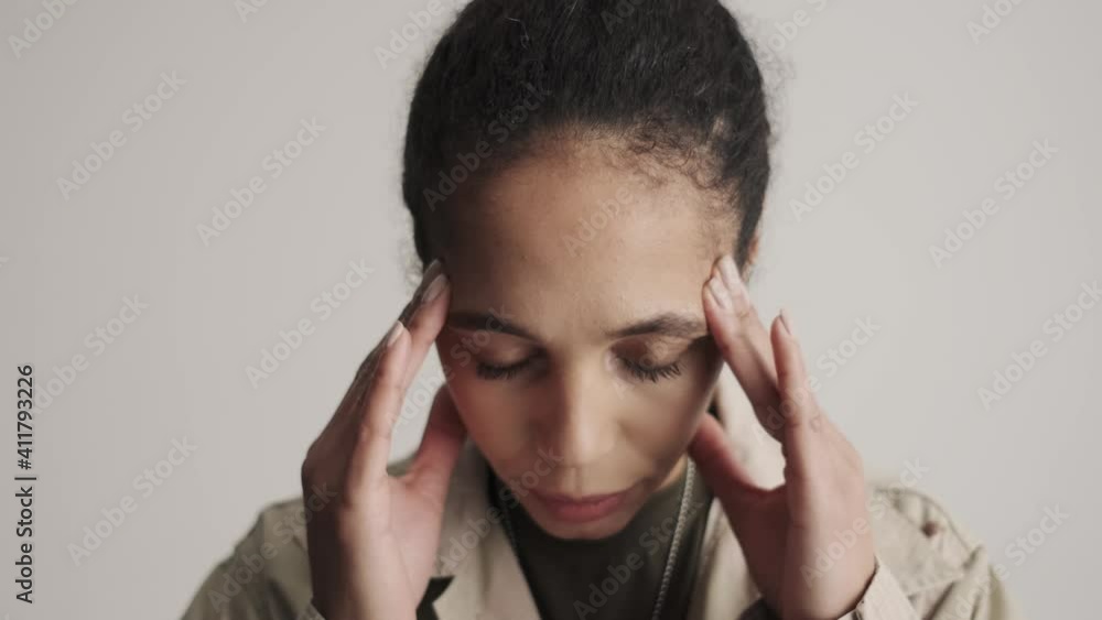 A close-up view of a nervous young american soldier woman is touching her temples standing isolated over a gray background in the studio A close-up view of a nervous young american soldier woman is touching her temples standing isolated over a gray background in the studio