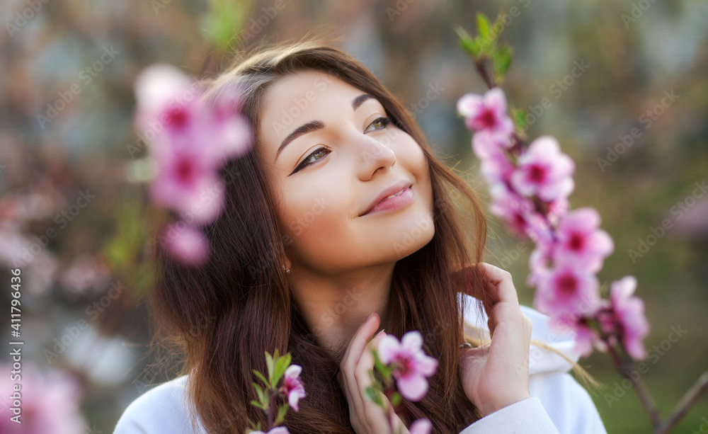 Smiling beautiful girl standing near a peach tree during sunset. Happy face. Spring time. Smiling beautiful girl standing near a peach tree during sunset. Happy face. Spring time.