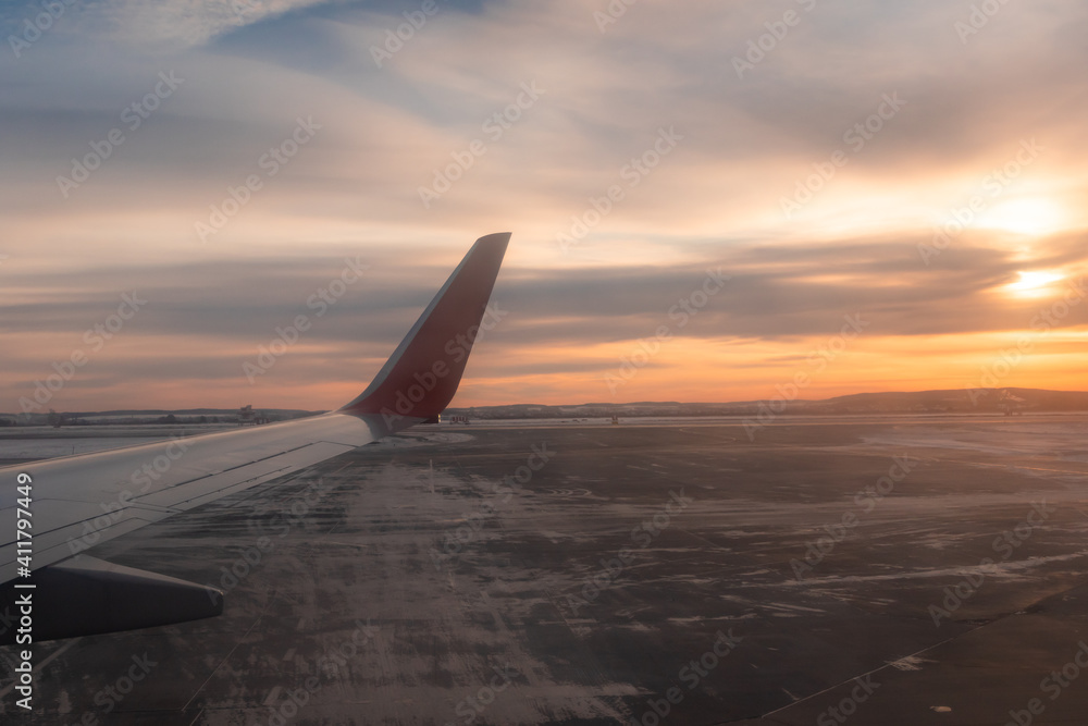 view from the window of an airplane taking off on the runway and the sky with clouds at dawn. part of an airplane wing in the frame