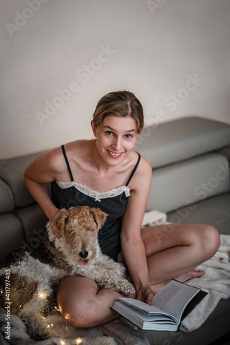 Smiling woman is reading a book next to her cute little fox terrier