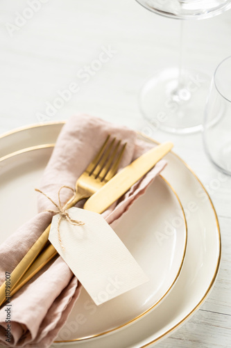 Golden rim plates and golden cutlery tied with blank tag on white table. Angle view on table setting  close up.