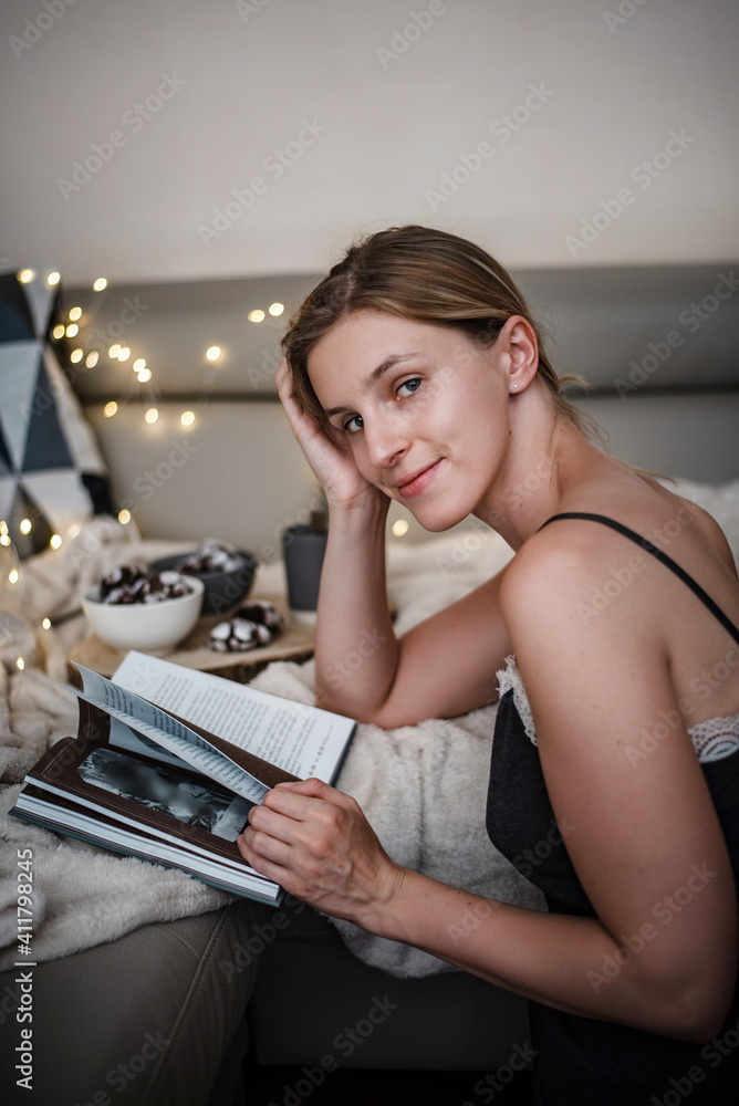 Holiday portrait of young woman smiling to camera while reading in her pyjamas. Holiday portrait of young woman smiling to camera while reading in her pyjamas.