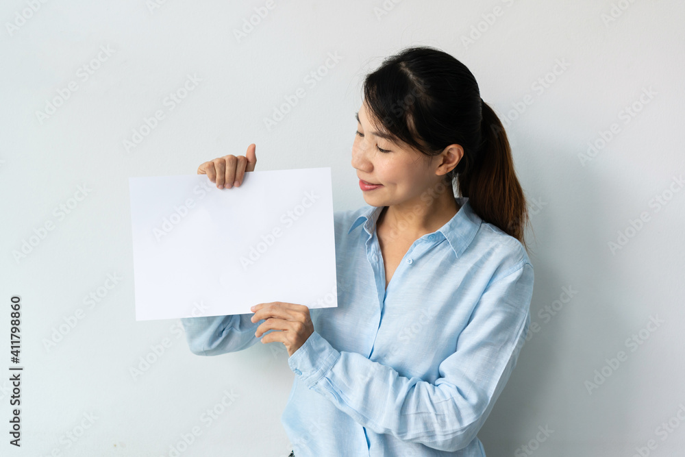 Beautiful young Asian woman in blue shirt holds a blank sheet of paper in hands for advertisement isolated over white background. Copy space. Beautiful young Asian woman in blue shirt holds a blank sheet of paper in hands for advertisement isolated over white background. Copy space.