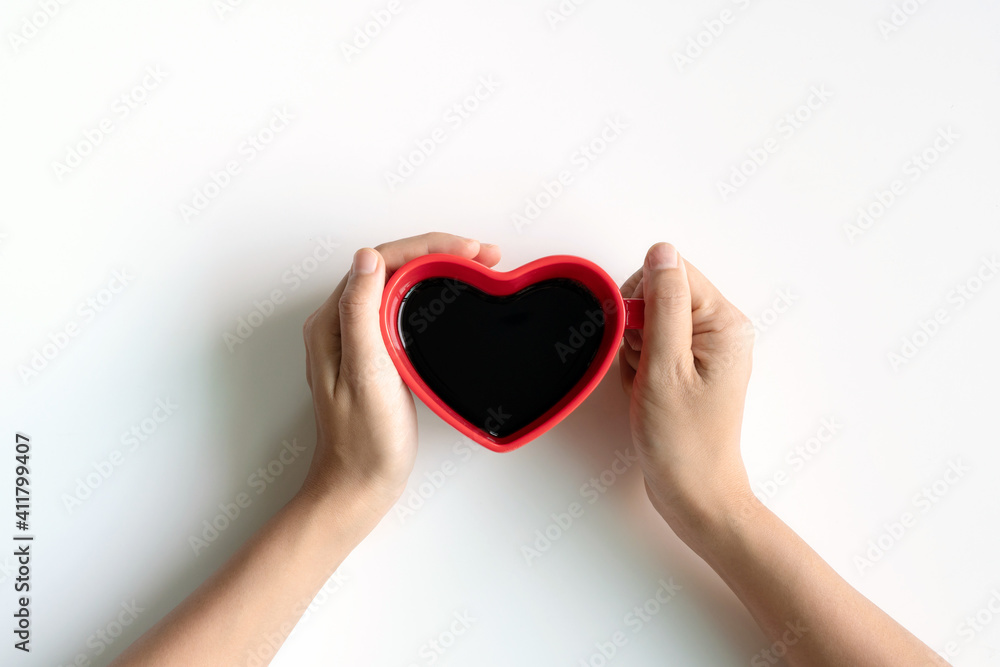 Fototapeta premium Flat lay of heart shaped cup of black coffee in the hands of women on a white desk with copy space. top view. Valentine, lifestyle concept
