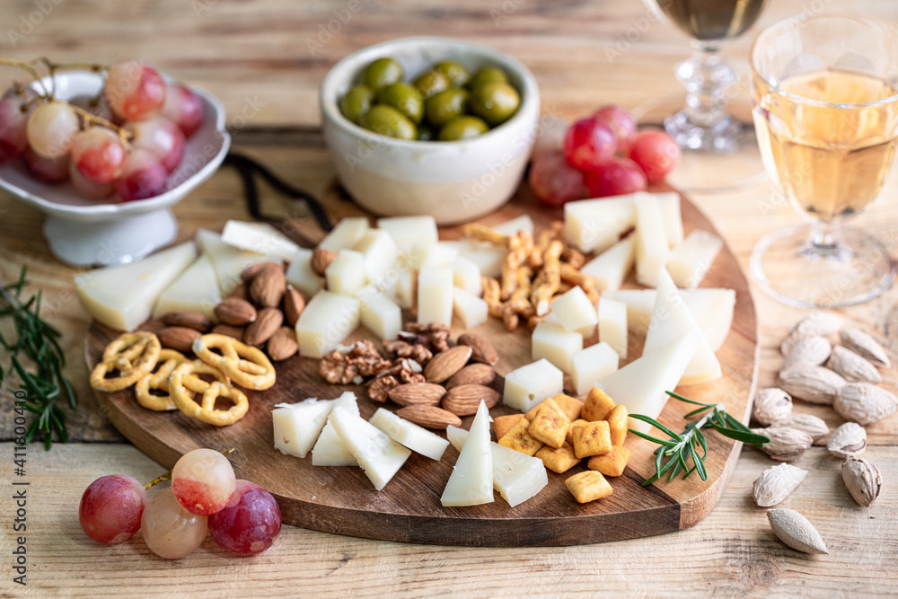 Assorted cheeses on a wooden cutting board in the shape of a heart. Cheese, grapes, walnuts, olives, rosemary and a glass of white wine.