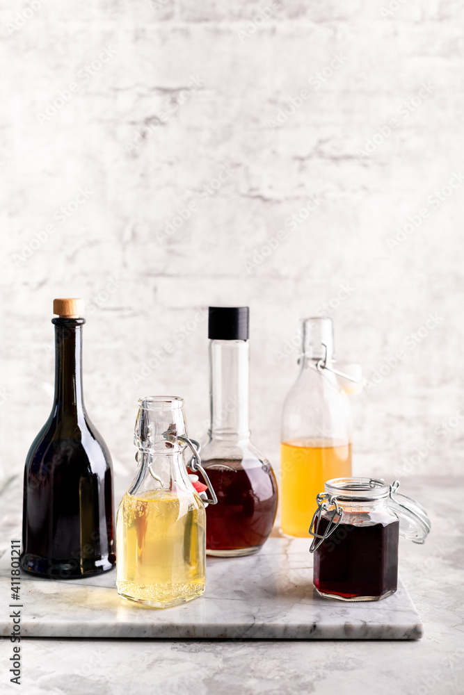 Original glass bottles with different vinegar on a marble table against a background of a white brick wall. Copy space. Original glass bottles with different vinegar on a marble table against a background of a white brick wall. Copy space.