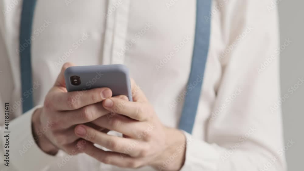 A close-up cropped view of a perfect man is using his mobile standing in the studio A close-up cropped view of a perfect man is using his mobile standing in the studio