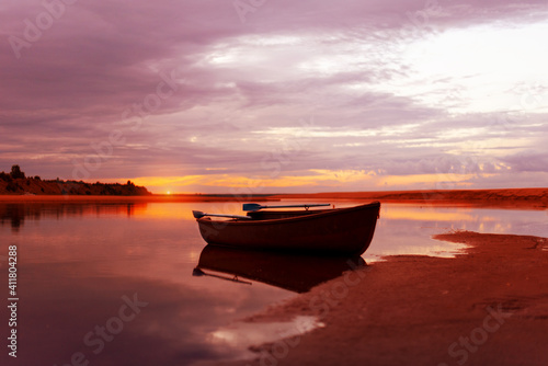 sunset over the river in pink and gold colors. There is a wooden boat with oars on the shore. countryside landscape