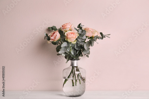 Fototapeta Naklejka Na Ścianę i Meble -  Vase with bouquet of beautiful roses on white wooden table near beige wall