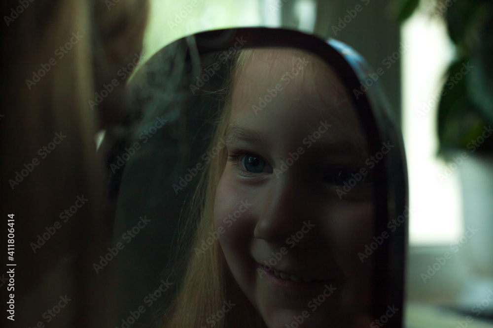 Little blond girl with blue eyes looking in the mirror. Cute serious curious child admires herself in reflection. Kids home portrait in daylight near window. Growing up psychology personal development Little blond girl with blue eyes looking in the mirror. Cute serious curious child admires herself in reflection. Kids home portrait in daylight near window. Growing up psychology personal development