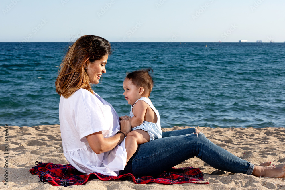 Smiling mom playing with newborn lying on beach towel
