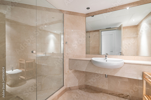 Interior of a peach bathroom in classic design  with shower zone  marble finishing and large mirror.