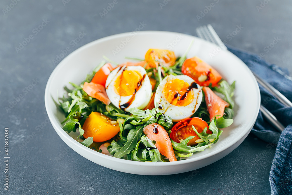 Healthy vegan salad of fresh tomato, arugula, salmon, egg and sesame on plate. Diet menu. Close-up Healthy vegan salad of fresh tomato, arugula, salmon, egg and sesame on plate. Diet menu. Close-up