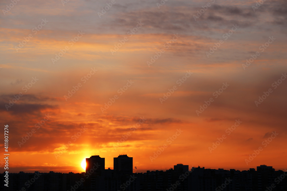 Sunset over city, scenic view. Setting sun and orange sky with dramatic clouds above silhouettes of residential buildings