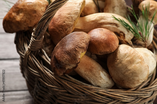 Fresh wild mushrooms in wicker basket on wooden table, closeup