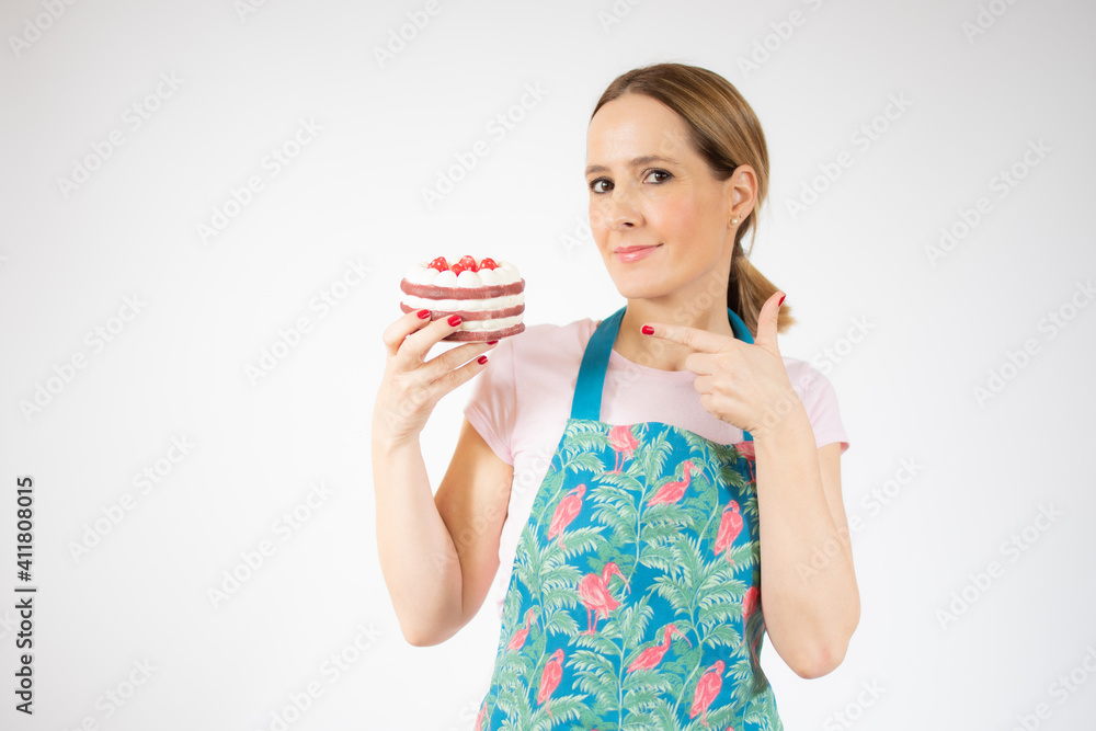 Smiling beautiful young woman wearing apron holding small cake over white background. Smiling beautiful young woman wearing apron holding small cake over white background.
