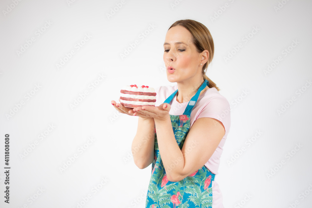 Smiling beautiful young woman wearing apron holding small cake over white background. Smiling beautiful young woman wearing apron holding small cake over white background.
