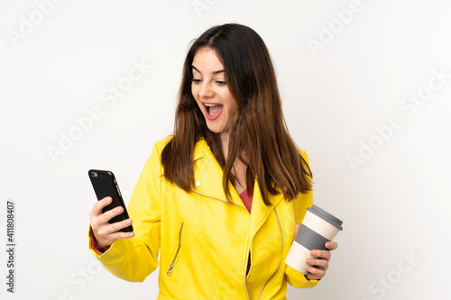 Young caucasian woman isolated on white background holding coffee to take away and a mobile