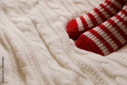 Woman in warm socks on knitted blanket, closeup. Space for text