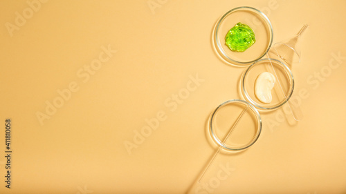Cosmetic skincare products in petri dishes on beige background. Aloe gel, moisturizer cream natural cosmetics for cosmetology in laboratory glassware. Top view Long web banner