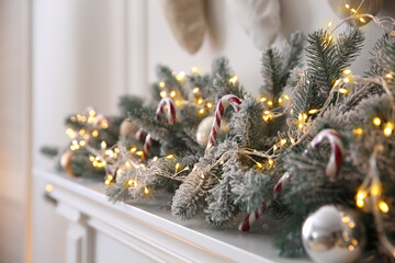 Beautiful decoration of fir tree branches, candy canes, fairy lights and Christmas balls in room, closeup