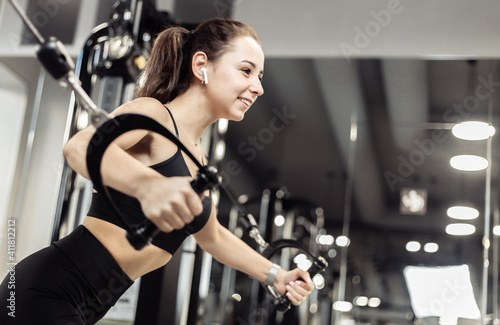 Young fit woman trains pectoral misci in a crossover exercise machine. Girl works out in modern gym