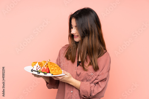 Young caucasian woman holding waffles isolated on pink background with happy expression