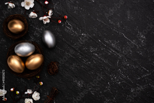 Golden and silver Easter eggs with flower on black background.