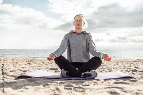 Attractive fit woman in sportswear meditates on the beach on a bright sunny day