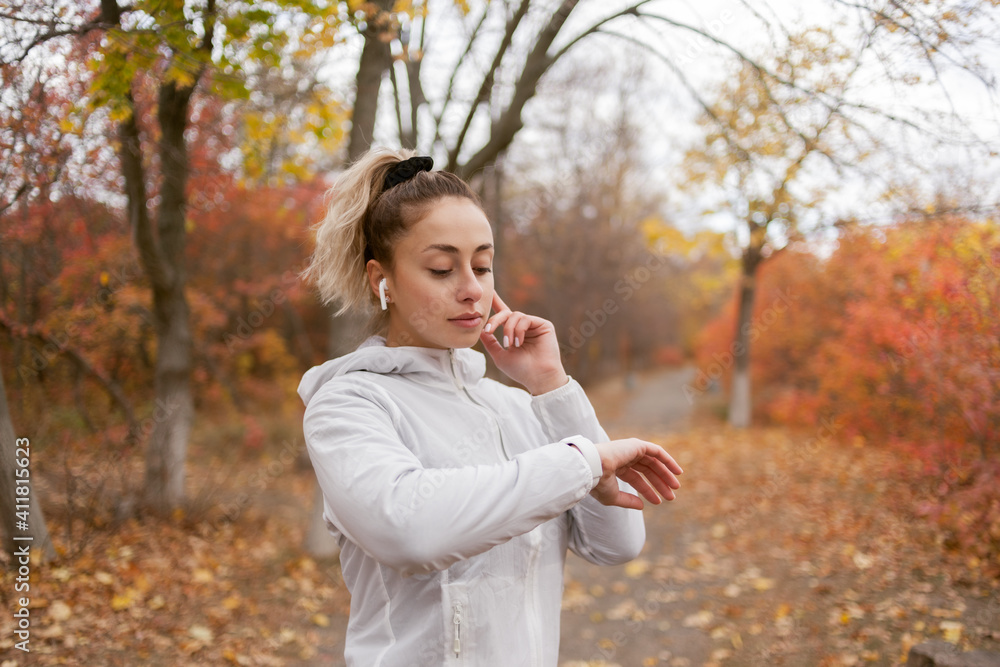 Fit woman in sportswear look at smart bracelet in the autumn forest. Listen music in headphones. Heart rate monitoring Fit woman in sportswear look at smart bracelet in the autumn forest. Listen music in headphones. Heart rate monitoring