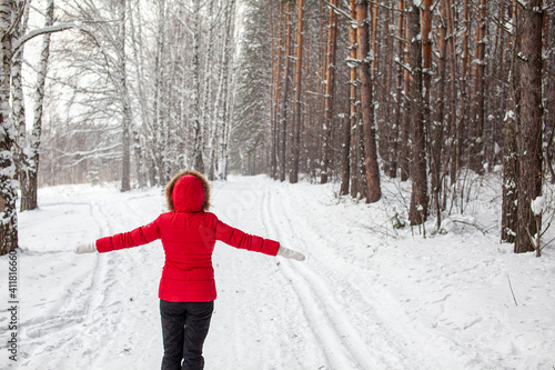 A girl in a red jacket walks through a snow-covered forest