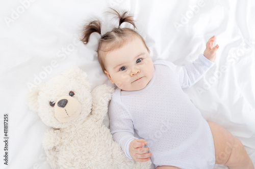 baby with a teddy bear lying on the bed at home, the concept of play and development of children