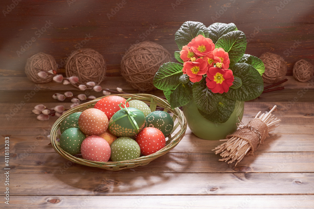 Red orange primrose flowers in the pot. Easter eggs and pussy willow twigs. Springtime decorations on rustic wooden background. Retro toned image of rustic Easter decorations. Sunlight with shadows. Red orange primrose flowers in the pot. Easter eggs and pussy willow twigs. Springtime decorations on rustic wooden background. Retro toned image of rustic Easter decorations. Sunlight with shadows.