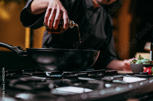 unrecognizable chef pouring oil into frying pan
