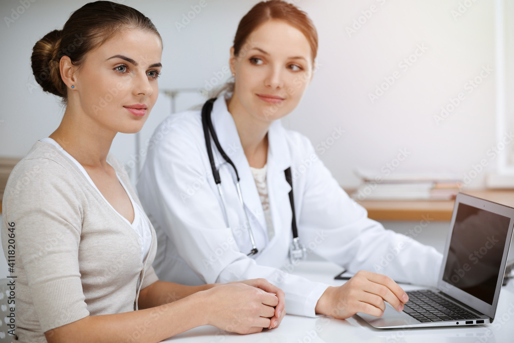 Doctor and patient are sitting and discussing health examination results while using laptop computer. Health care, medicine and good news concepts Doctor and patient are sitting and discussing health examination results while using laptop computer. Health care, medicine and good news concepts