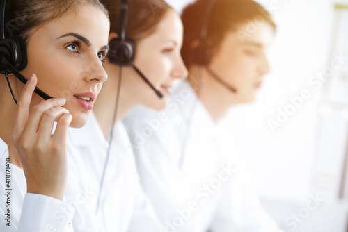 Call center. Beautiful young woman using headset and computer to help customers in sunny office. Business concept
