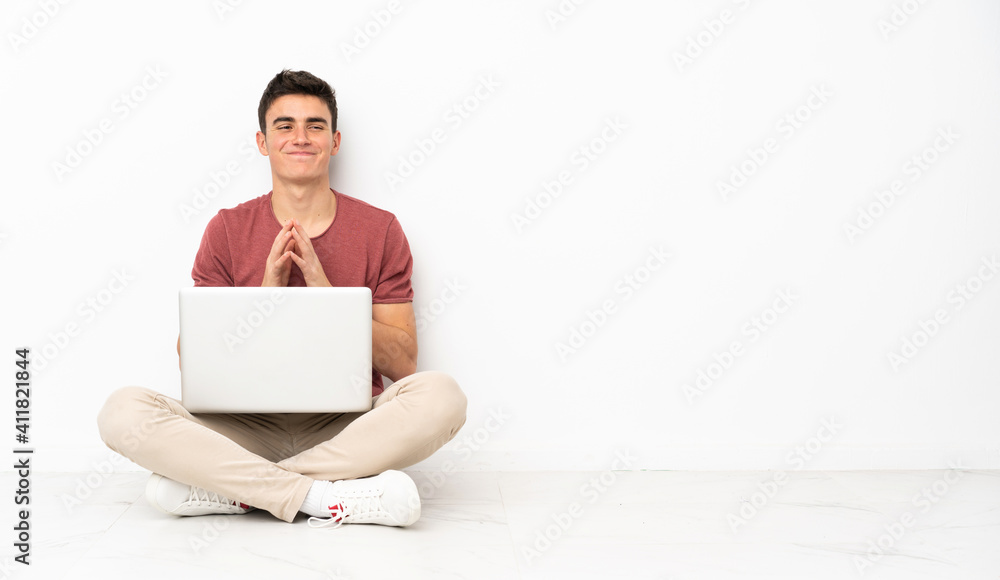 Teenager man sitting on the flor with his laptop scheming something Teenager man sitting on the flor with his laptop scheming something
