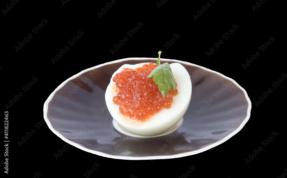 Red caviar on half egg and saucer isolated on black Red caviar on half egg and saucer isolated on black