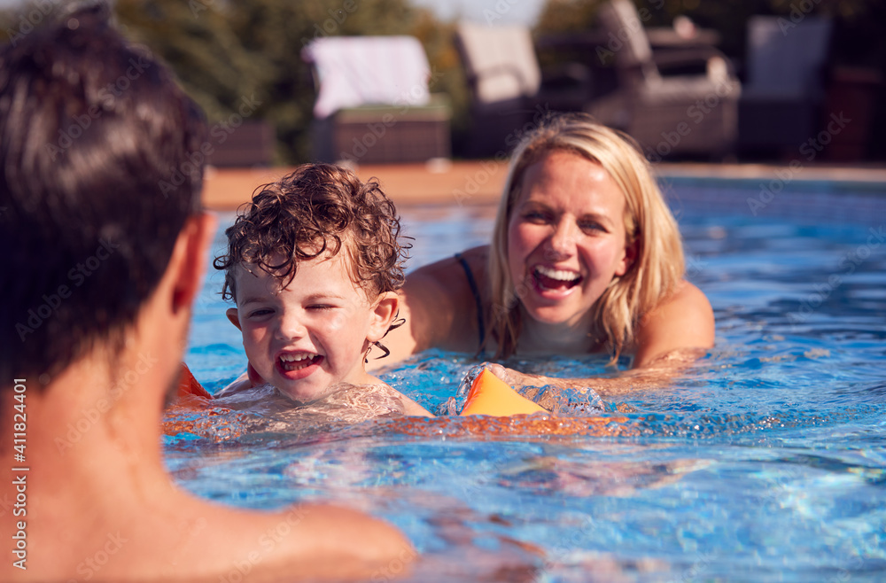 Family In Outdoor Pool On Summer Vacation Teaching Son To Swim With Inflatable Armbands Family In Outdoor Pool On Summer Vacation Teaching Son To Swim With Inflatable Armbands