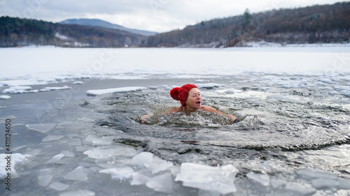 Front view of active senior woman in swimsuit outdoors in water in winter, cold therapy concept.
