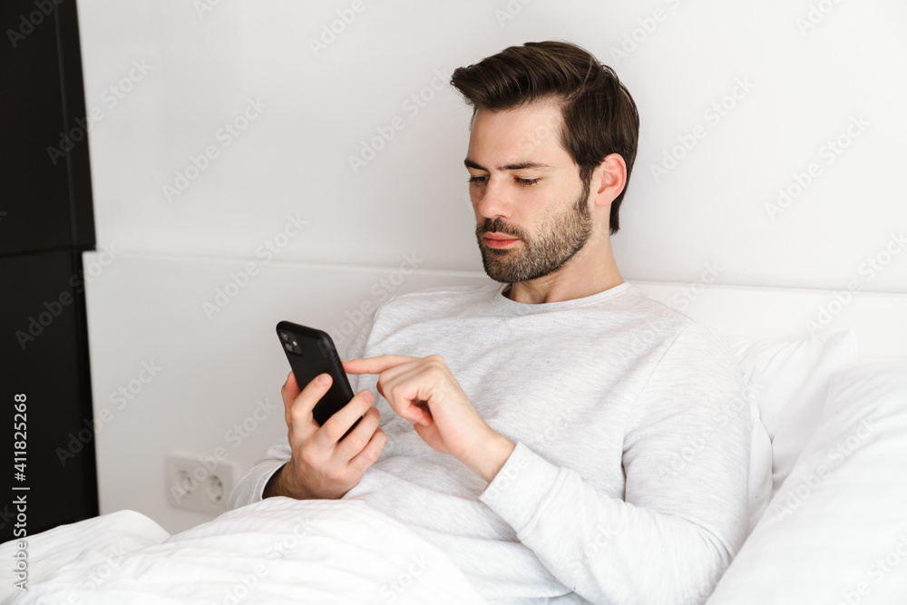 Focused handsome man using mobile phone while resting in bed Focused handsome man using mobile phone while resting in bed