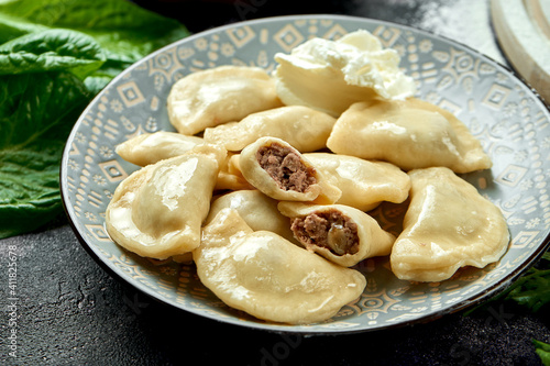 Ukrainian or Polish traditional dish - Pierogi or Varenyky (dumplings) stuffed with meat and sour cream. dark background. Close up, selective focus