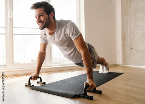 Joyful athletic man doing exercise with push-up stops while working out photo