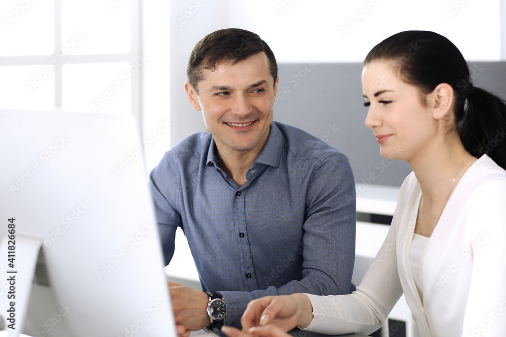 Obraz premium Cheerful smiling businessman and woman working with computer in modern office. Headshot at meeting or workplace. Teamwork, partnership and business concept
