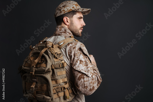 Confident masculine military man in uniform posing with backpack